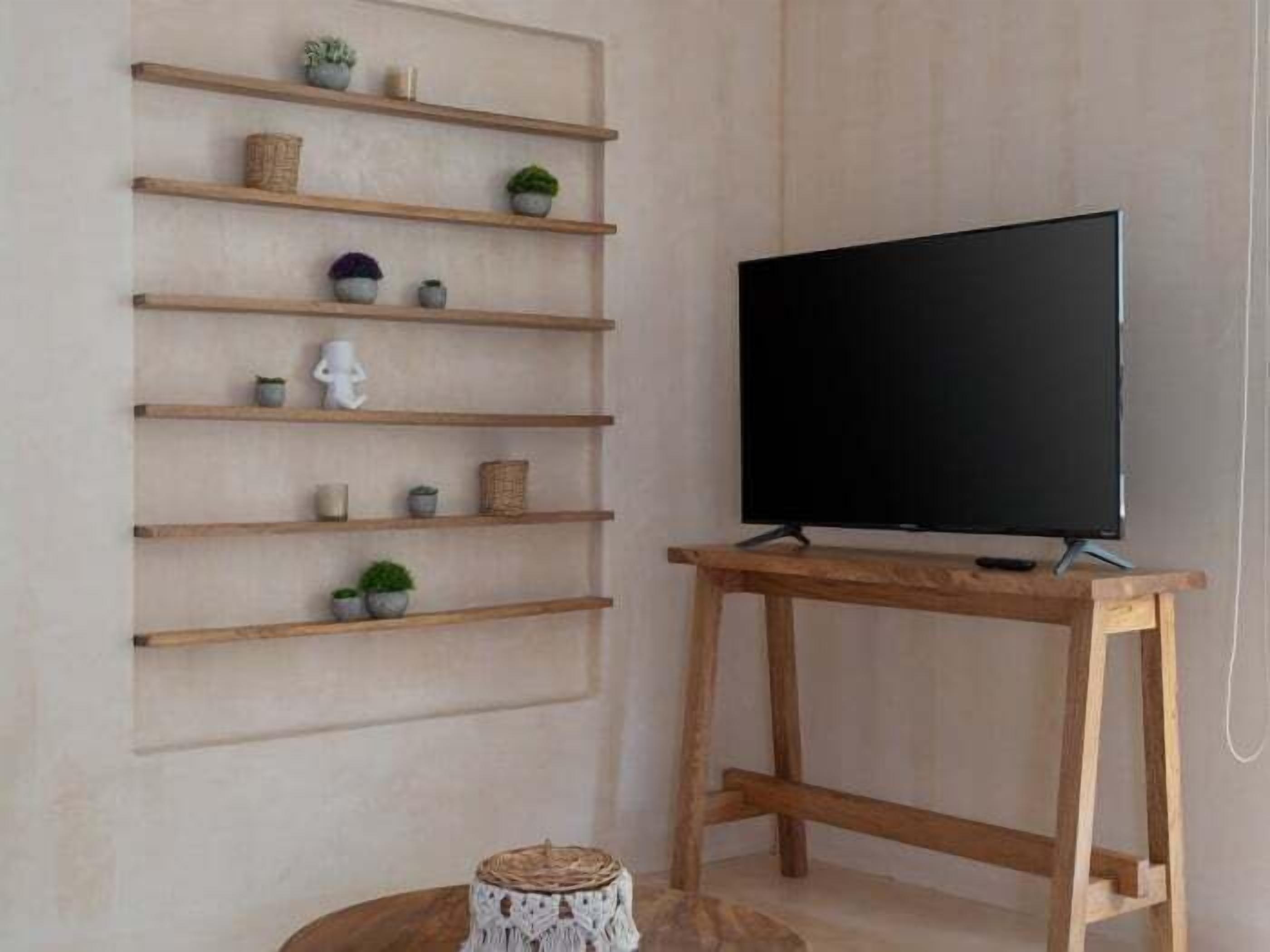 Un salon avec un meuble TV en bois et une étagère murale où sont exposés divers objets décoratifs.