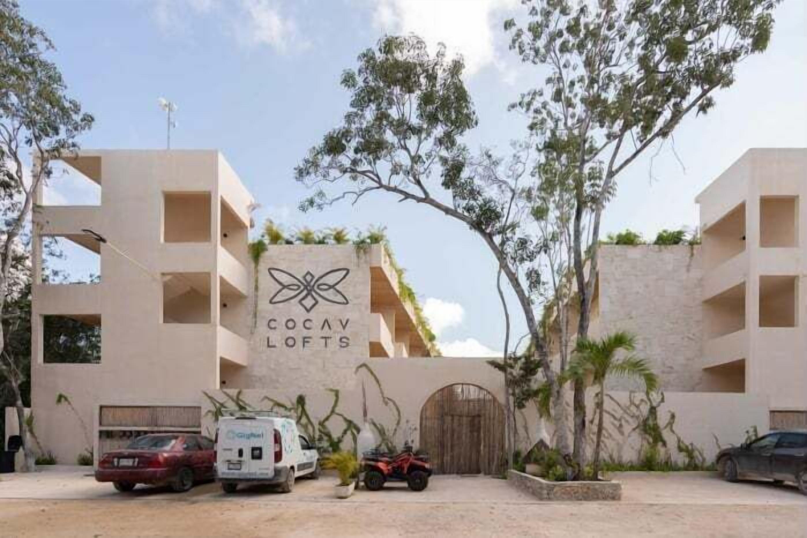 Edifici modern amb un rètol que diu "Cocav Lofts". Hi ha diversos vehicles estacionats al davant, incloent-hi una furgoneta blanca i un cotxe vermell.