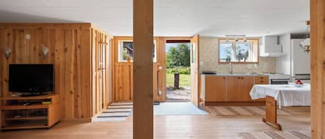 A modern interior with wooden walls, a TV, a kitchen, and a view to the outdoors.