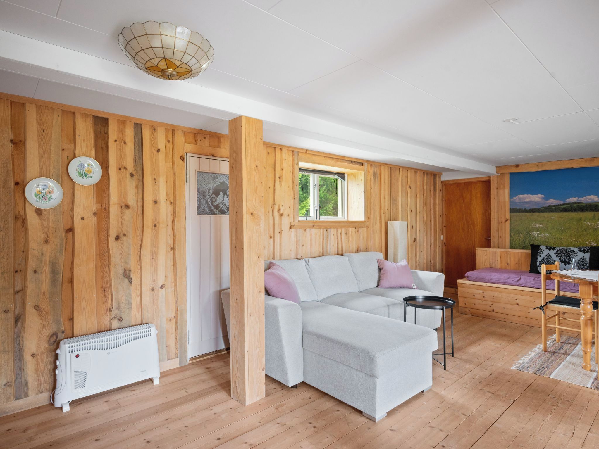 Une pièce aux murs en bois, avec un canapé blanc, une petite table et un radiateur.