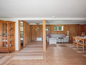 A spacious living area with a wooden floor, a white sofa, a wooden cabinet, and a dining table with chairs.