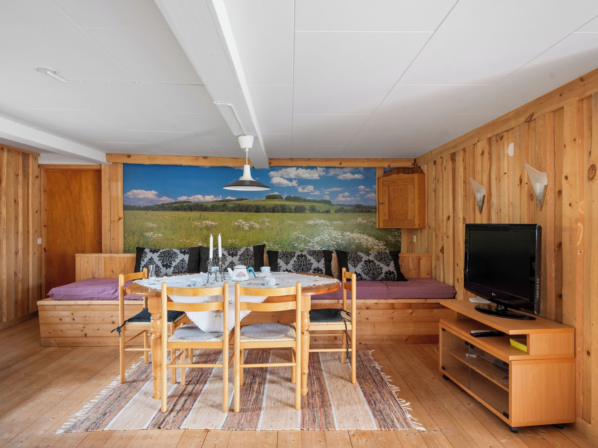 Ett mysigt rum med träinredning, ett runt matbord, en soffa och en tv.