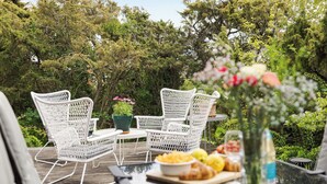An outdoor seating area with white wicker chairs and a table, surrounded by lush greenery. - Ringenäs by Interhome (Halmstad)