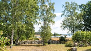Ett grönområde utomhus med träd, en stenmur och utsikt över en vattenyta.