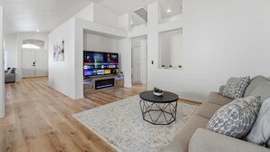 Een moderne woonkamer met een flatscreen televisie, een ronde salontafel en een bank met gekleurde kussens.