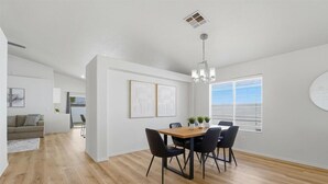 Een moderne eetruimte met een houten tafel en zwarte stoelen, witte muren en een groot raam met jaloezieën.