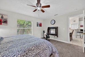 A bedroom with a bed, a desk, a chair, a ceiling fan, a window with blinds, and a wall clock. - Tiger Bay Park Daytona Tranquility Home (Daytona Beach)