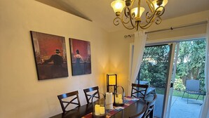 A dining area with a dark wooden table, six chairs, a chandelier, and two paintings on the wall.