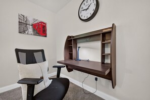 Une pièce comprenant un bureau, une chaise, une horloge et une étagère fixée au mur.