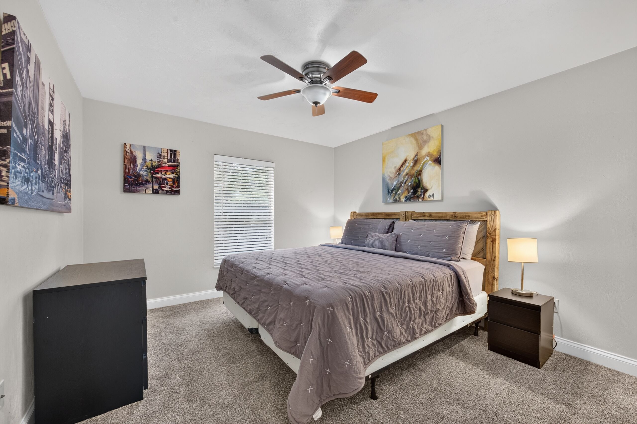 Une chambre à coucher avec un lit, un ventilateur de plafond, une table de chevet, une lampe et des œuvres d’art accrochées aux murs.