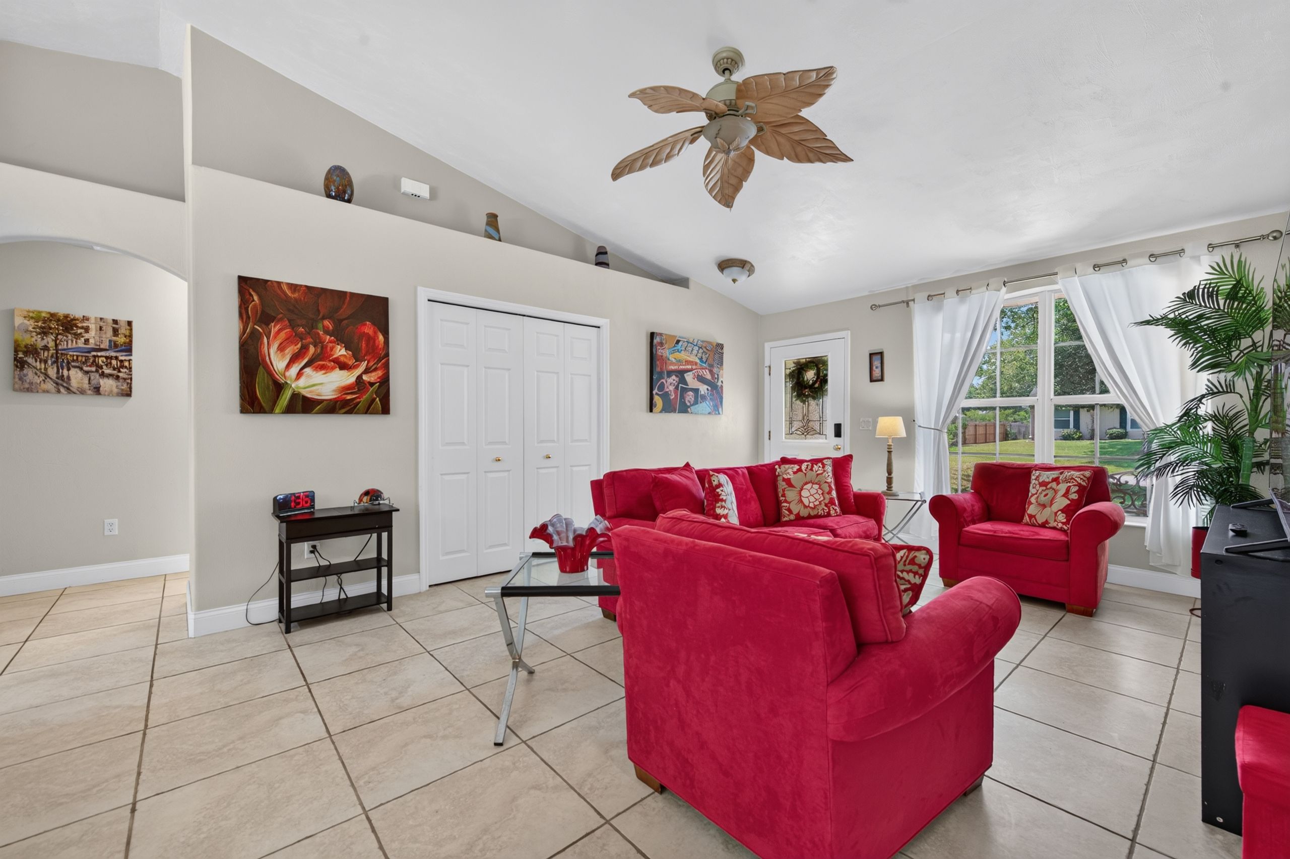 A spacious living room with red sofas, a ceiling fan, and artwork on the walls.