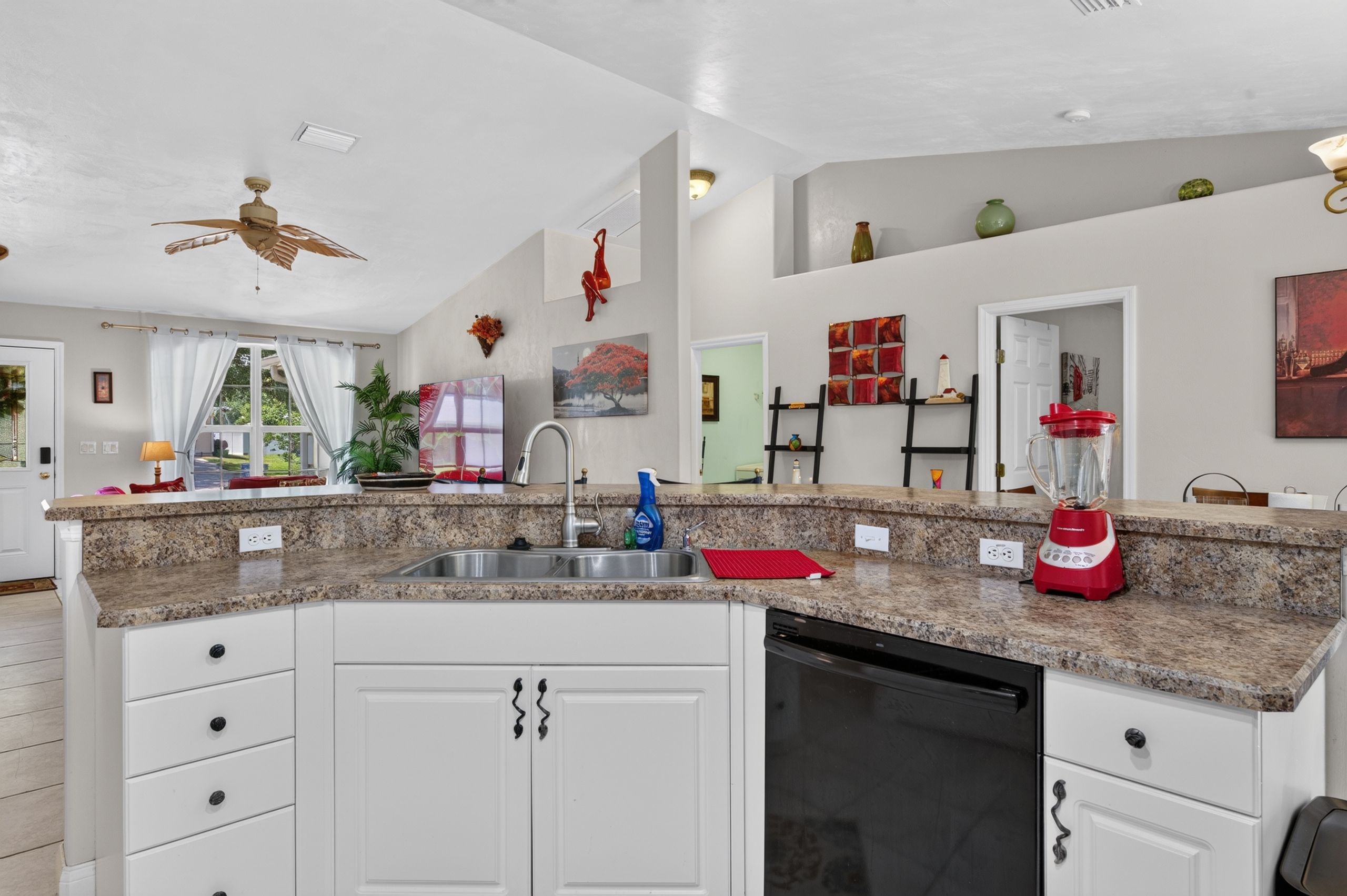A kitchen with granite countertops, white cabinetry, a built-in dishwasher, and a ceiling fan.