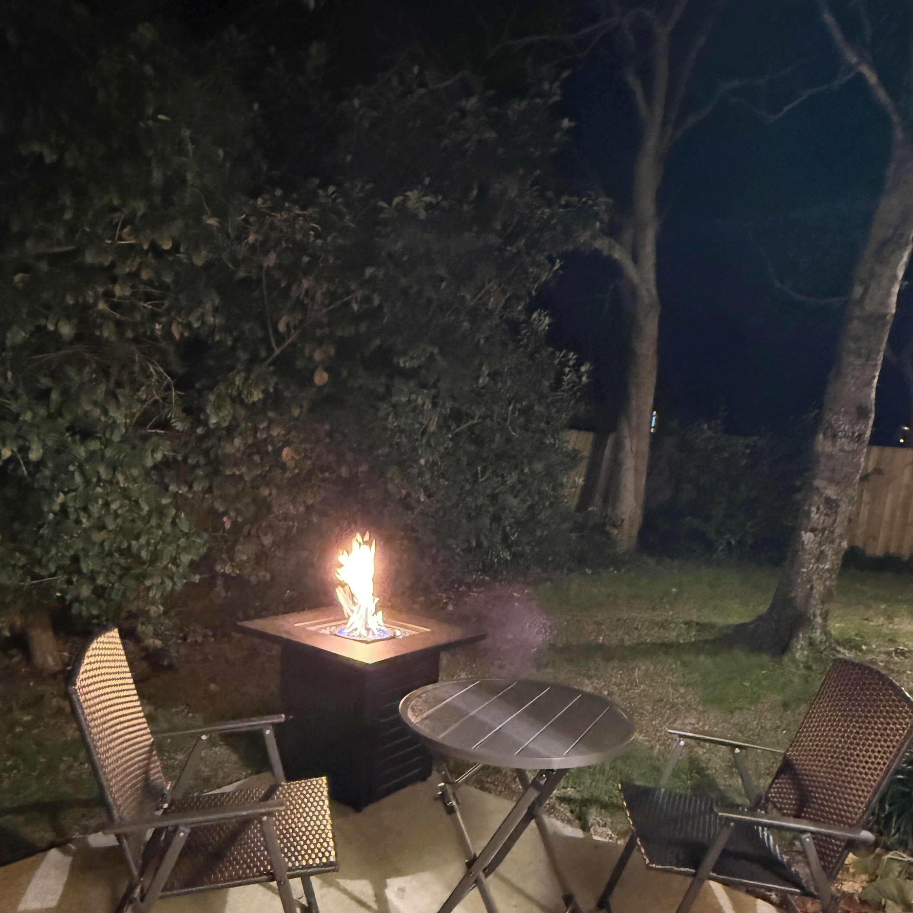 Un patio con una chimenea, dos sillas y una mesa.