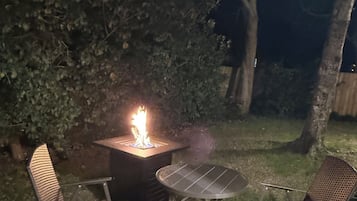 Un patio con una chimenea, dos sillas y una mesa.