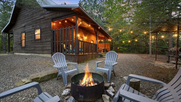 Een rustieke blokhut met een vuurkorf en Adirondack-stoelen.