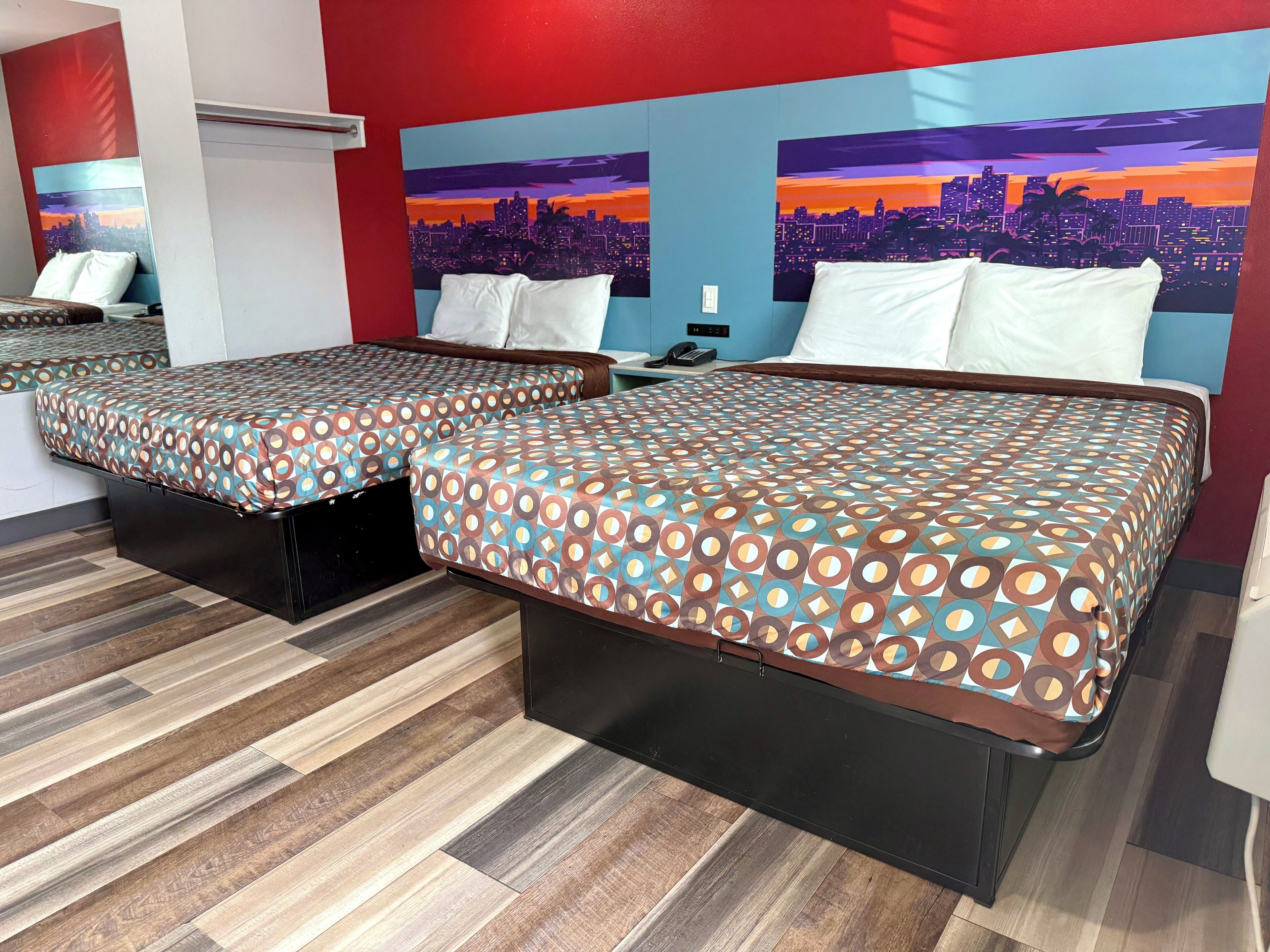 A hotel room with two beds, a cityscape mural on the wall, and a wooden floor.