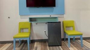 A room with a flat-screen TV mounted on the wall, a small black refrigerator, and two yellow chairs with blue frames. - La Casa Motel Burbank Airport - LA (Sun Valley)