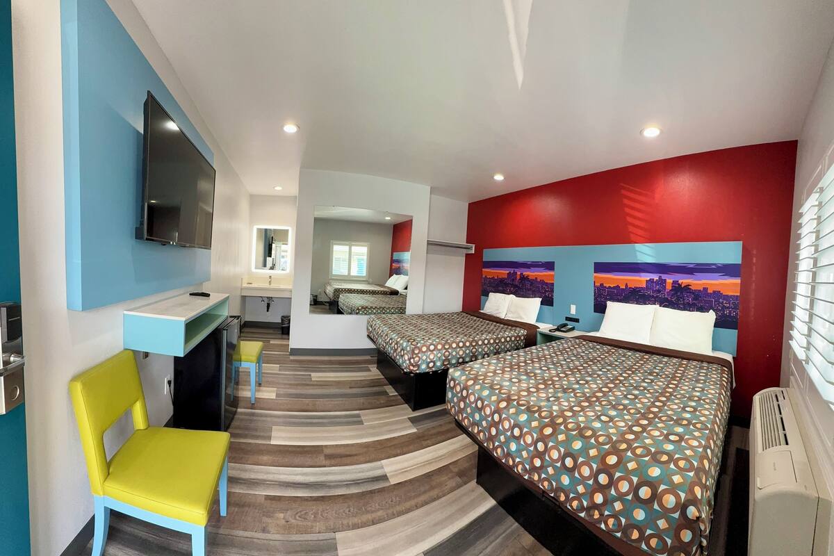 A hotel room with two beds, a desk, a chair, and a TV.