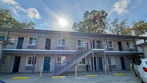 A multi-story motel with a central staircase, individual rooms on each floor, and a parking area with a white car. - La Casa Motel Burbank Airport - LA (Sun Valley)