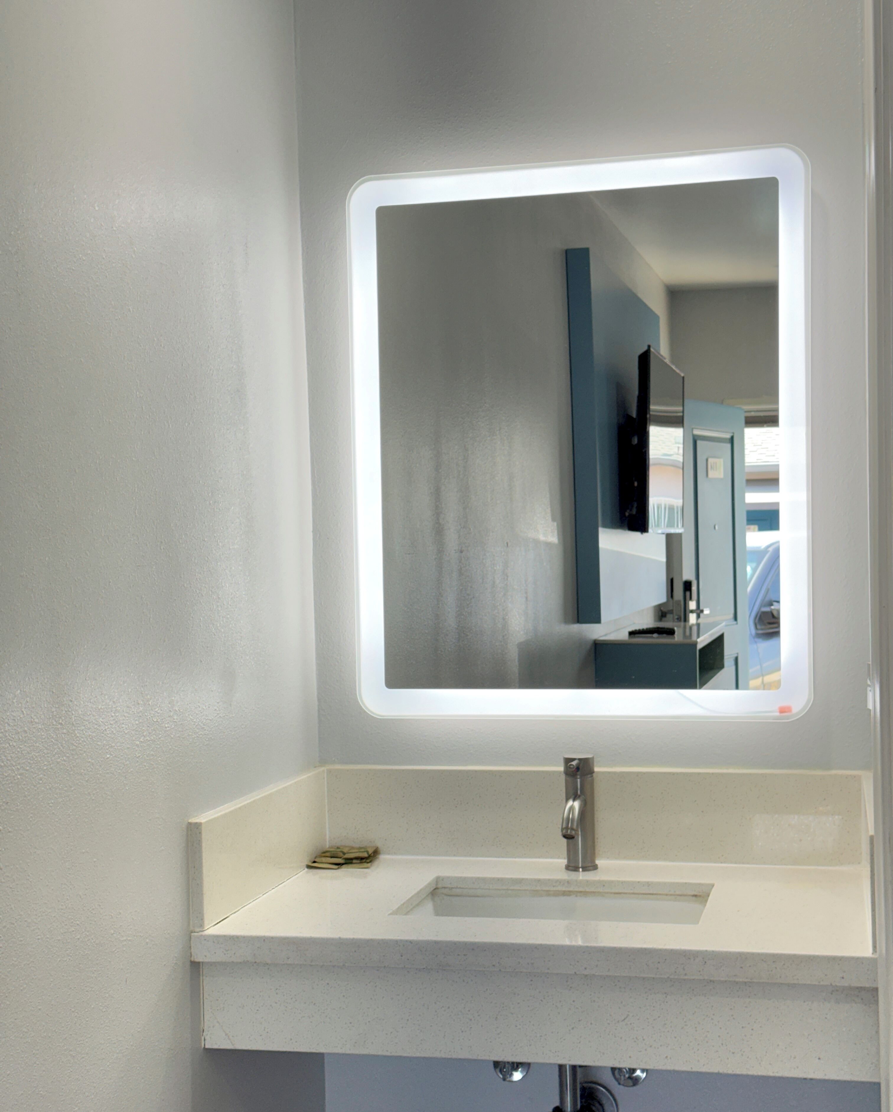 A bathroom with a white sink, a mirror with a light, and a blue door in the background.