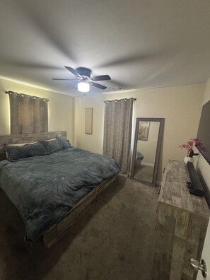 Un dormitorio con cama, ventilador de techo, espejo y cómoda.