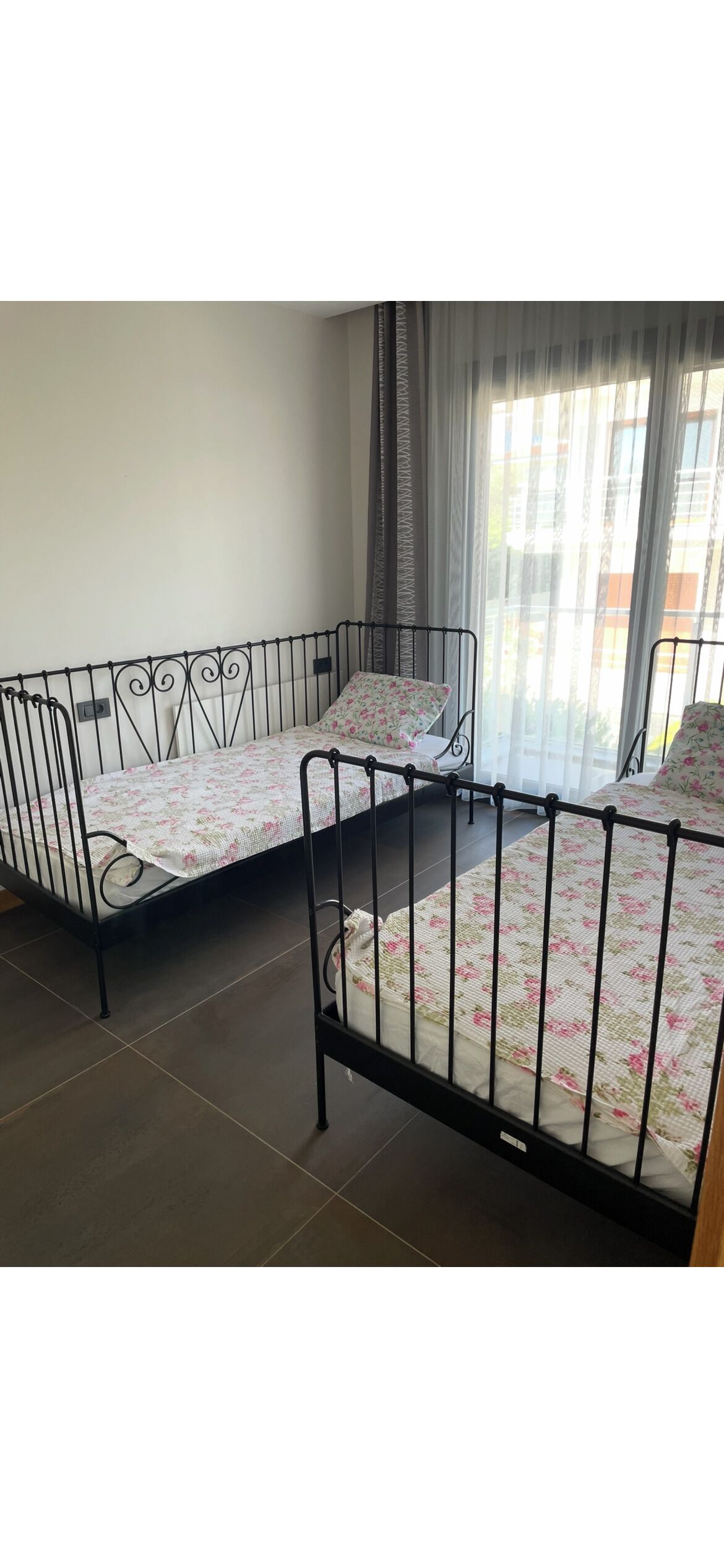 Two metal bunk beds with floral bedding in a room with a large window and curtains.
