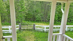 A covered porch with white railings and a view of a grassy area with a white fence and trees.