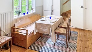 A room with a wooden bench, a table set for dining, a window with curtains, a radiator, and a staircase.