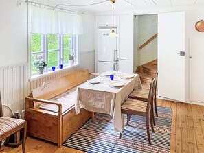 Ein Zimmer mit einer hölzernen Bank, einem Esstisch, einem Fenster mit Vorhängen, einem Heizkörper und einer Treppe.
