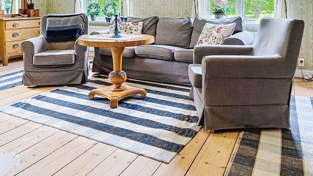 A living room with a sofa set, a round wooden table, and a striped rug.