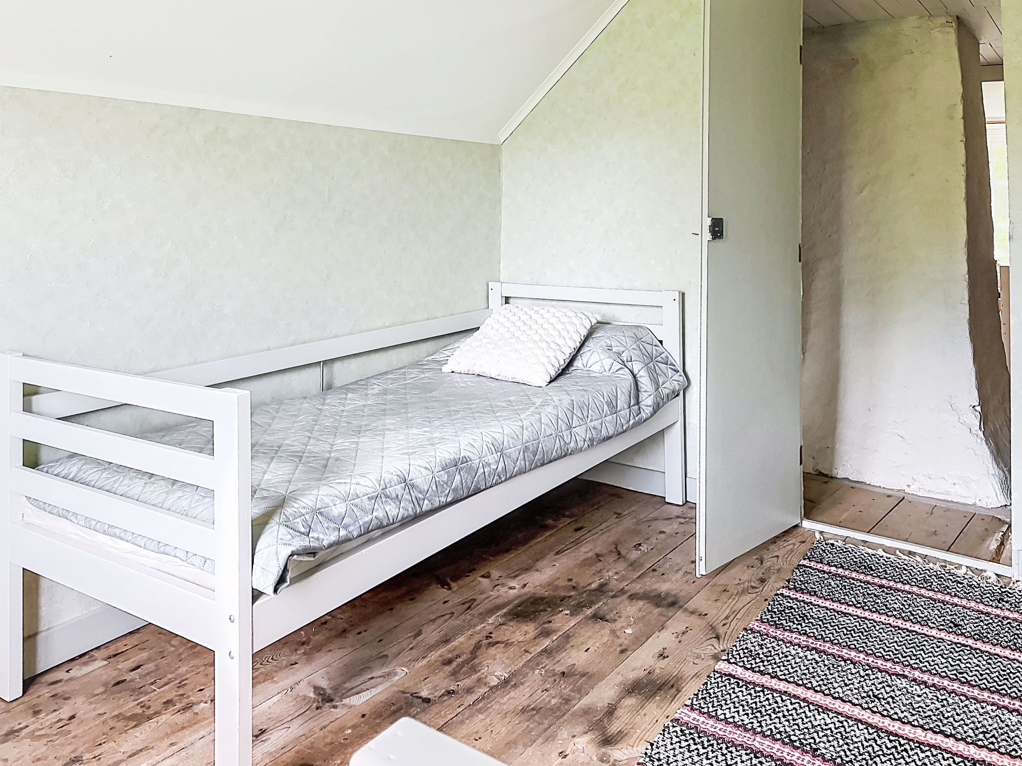 A small, single-bed room with a wooden floor and a simple, white bed frame.