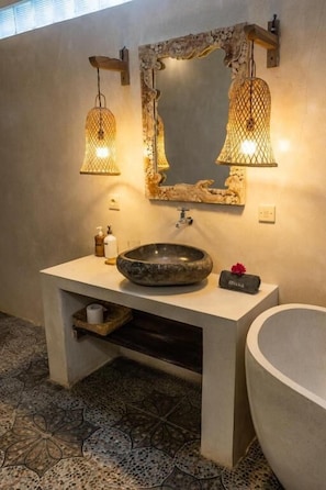 Un baño con un lavabo de piedra, un espejo grande y dos luces fijadas a la pared.