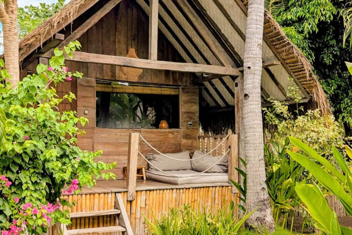 Una cabaña de madera con techo de paja, una terraza de madera y una hamaca.