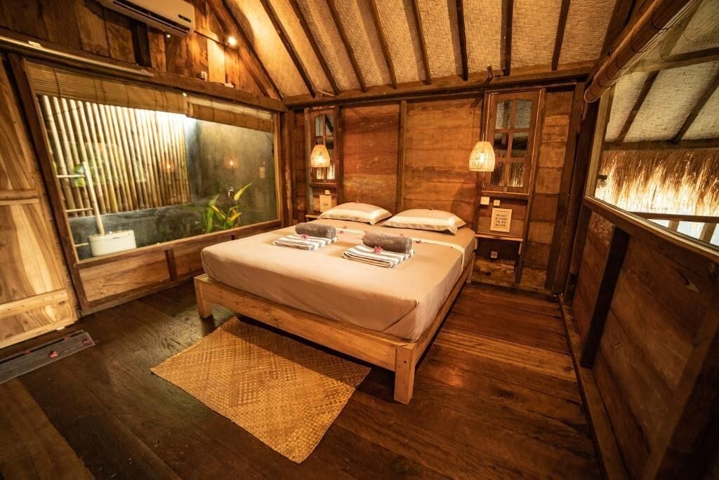 A wooden room with a bed, a window, and a small table.