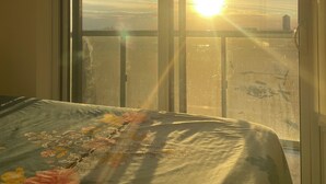 A room with a large window, a bed with a floral bedspread, and a view of the sunset.