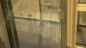 A view from a high-rise building with a glass door, overlooking a cityscape during sunset.