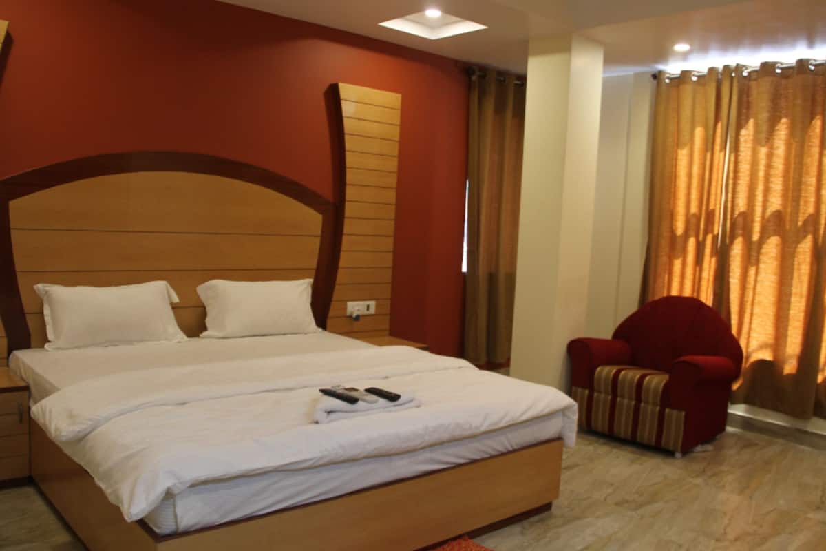 Quarto de hotel com uma cama grande, uma poltrona vermelha e uma janela com cortinas.