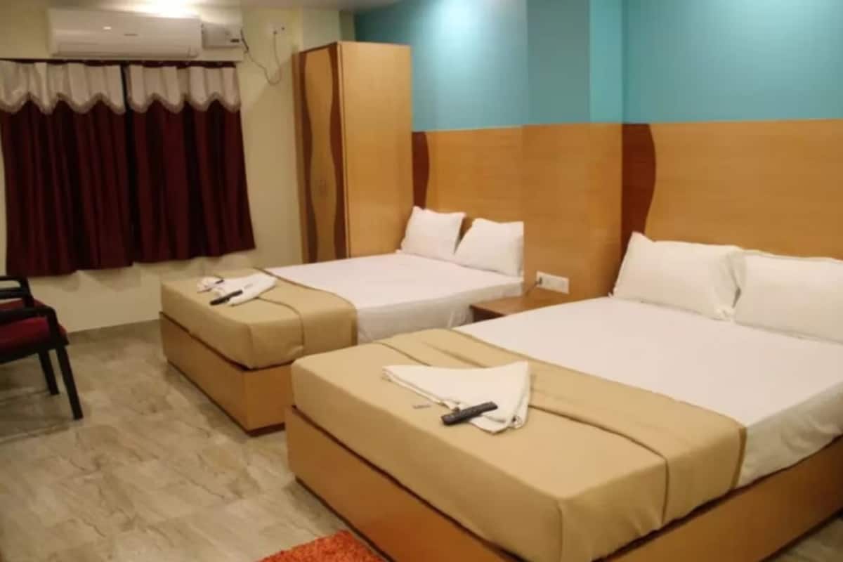 Quarto de hotel com duas camas, um guarda-roupa, uma cadeira e um ar condicionado.