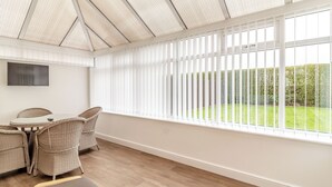 A conservatory with a glass ceiling, wicker furniture, a flat-screen TV, and a view of a well-maintained garden. - 4 bedroom accommodation in Sea Palling (Sea Palling)
