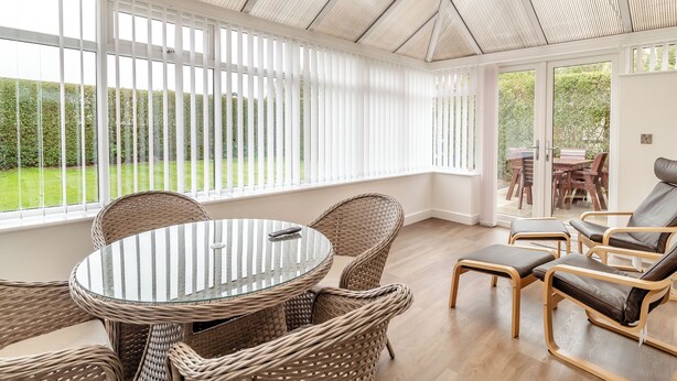 A conservatory with wicker furniture, a glass table, and a view of a garden. - 4 bedroom accommodation in Sea Palling (Sea Palling)