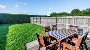 A wooden deck with a table and chairs, surrounded by a neatly trimmed lawn and a wooden fence.