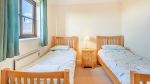 A bedroom with two wooden beds, a nightstand with a lamp, a window with curtains, and a radiator.
