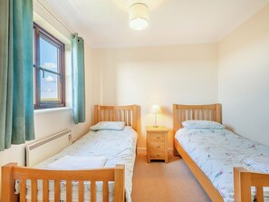 Un dormitorio con dos camas de madera, una mesita de noche con una lámpara, una ventana con cortinas y un radiador.