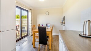 A modern kitchen with wooden flooring, a dining table with chairs, a built-in oven, and a large window with a view of the outdoors.