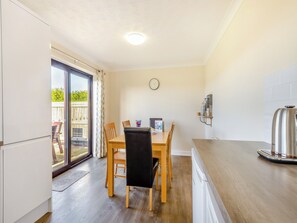 Una cocina moderna con suelo de madera, una mesa de comedor con sillas, horno empotrado y un amplio ventanal con vistas al exterior.