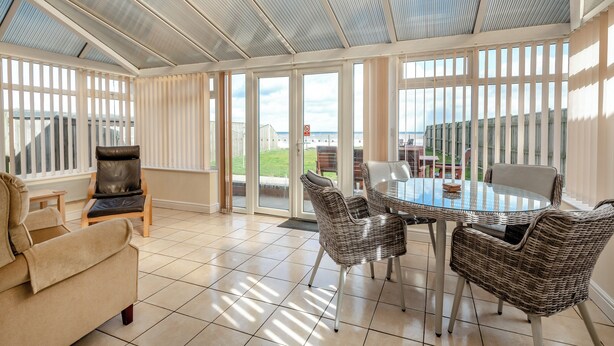 Una veranda con tetto in vetro, un tavolo da pranzo con sedie, un divano e vista sul mare.
