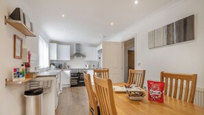 A modern kitchen with white cabinets, a built-in oven, and a dining area with wooden chairs and a table. - 4 bedroom accommodation in Sea Palling (Sea Palling)