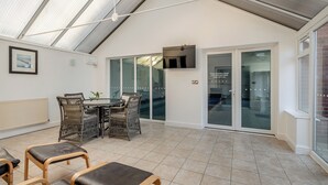 A spacious patio with a dining table and chairs, a TV mounted on the wall, and a sliding glass door leading to an indoor area. - 4 bedroom accommodation in Sea Palling (Sea Palling)