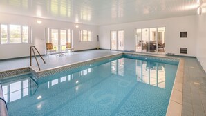 An indoor swimming pool with clear blue water, a tiled floor, and a ceiling with horizontal lines. There are windows on one side and a door leading to another room. - 4 bedroom accommodation in Sea Palling (Sea Palling)