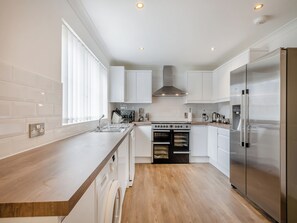 A modern kitchen with white cabinetry, a stainless steel refrigerator, a built-in oven, and a dishwasher. - 4 bedroom accommodation in Sea Palling (Sea Palling)